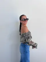 Top corto negro con diseño de encaje floral en blanco, escote bardot y mangas largas acampanadas.