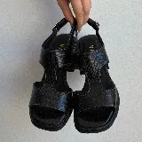 Sandalias de cuero vacuno color marrón con textura tipo cocodrilo, taco ancho y plataforma. Diseño con puntera descubierta y tira ancha sobre el empeine con aberturas laterales. Cierre con hebilla en el tobillo.