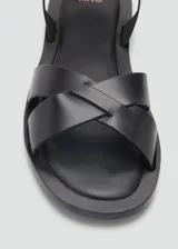 Sandalias planas negras de cuero con tiras cruzadas en el empeine y tira con hebilla en el tobillo.