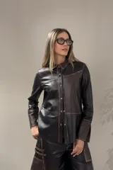 Camisa de cuero con diseño de patchwork en tonos negro y marrón oscuro, con efecto desgastado en las costuras. Presenta cuello camisero, botones frontales y mangas largas.