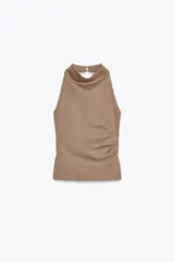 Top color beige de cuello halter y hombros descubiertos, con espalda descubierta, bajo con aberturas laterales y cierre en cuello con botones.