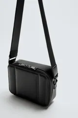 Bandolera negra acolchada con correa ajustable. Tiene un compartimento principal con cierre de cremallera, un bolsillo plano interior y tres compartimentos para tarjetas.