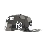 Gorro tipo snapback Supreme x New Era, con diseño de camuflaje en tonos grises y blancos. Presenta el logo Box Supreme en el frente y el logo de los New York Yankees bordado en blanco en el lateral.