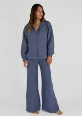 Chaqueta azul de lino con cuello camisero, cierre frontal con botones, mangas largas con puños abotonados, dos bolsillos de parche en el pecho y bajo con terminación desflecada.