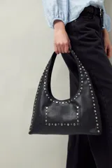 Cartera negra tipo hobo de cuero sintético con apliques de tachas metálicas plateadas en el frente y los bordes.