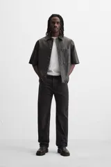 Sobrecamisa negra de manga corta confeccionada en tejido efecto piel, con cuello solapa, bolsillo frontal de parche y cierre frontal con botonadura oculta.