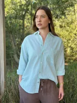 Camisa holgada a rayas verticales color beige y blanco, con cuello clásico, manga larga, bolsillo en el pecho y cierre frontal con botones nacarados.