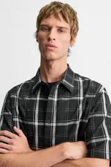 Camisa de hombre relaxed fit con estampado de cuadros blancos sobre fondo negro, cuello solapa, manga corta y cierre frontal con botones.