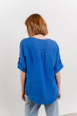 Camisa azul de lino con escote en V abotonado, bolsillo frontal y mangas 3/4 con trabilla.
