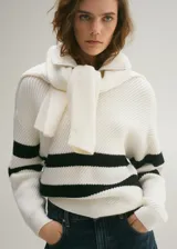 Sweater de punto grueso color blanco con rayas horizontales negras, cuello alto con cremallera y mangas largas.