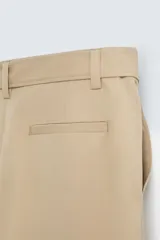 Pantalón negro de corte amplio con cinturón de tela con hebilla metálica. Presenta pliegues frontales, bolsillos laterales y traseros. Cierre frontal con cremallera y botón.
