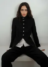 Chaqueta negra entallada con cuello mao y cierre frontal con botones plateados.