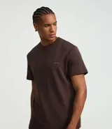 Remera deportiva marrón de corte clásico, cuello redondo y mangas cortas. Confeccionada en tejido de poliéster y modal con tecnología Dry, que facilita la transpiración. Presenta un pequeño estampado con lettering en el pecho.
