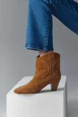 Bota corta de gamuza color camel, estilo cowboy, con taco medio de madera y recortes grabados en forma de mariposa en los laterales.