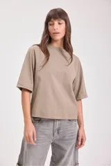 Camiseta de manga corta ancha, color beige topo, con cuello redondo y corte ligeramente holgado.