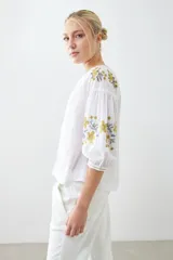 Blusa blanca de estilo boho con bordados de flores en amarillo y azul en mangas y escote.