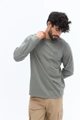 Remera de manga larga color verde militar, con escote redondo y un pequeño logo circular estampado en el pecho.