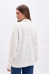 Buzo de tejido de punto color blanco roto, con cuello polo y medio cierre frontal. Presenta una banda horizontal en el pecho con el texto "ATHLETIC CLUB" en color rojo.