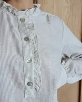 Camisa a rayas verticales color beige y blanco, de corte holgado, con cuello con volados, cierre parcial con botones y mangas largas con puños abotonados.