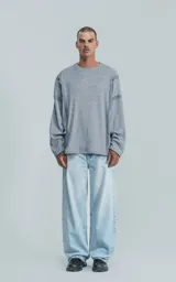 Sweater de manga larga color gris jaspeado, con cuello redondo. Presenta costuras externas decorativas y marcadas en los laterales del cuerpo y en la unión de las mangas, dándole un aspecto técnico o deconstruido.