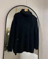 Sweater negro de cuello alto con botones decorativos en los laterales. Corte oversize y mangas largas caídas.