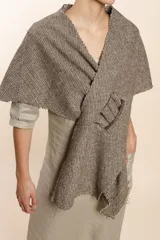 Chal asimétrico de lana color gris claro, con cortes en los hombros y doble ojal de fieltro para mantener el cruce. Terminación pespunteada y al corte.