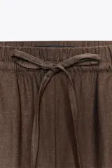 Pantalón blanco de lino, de corte ancho y tiro medio, con cintura elástica ajustable con cordones y bolsillos laterales.