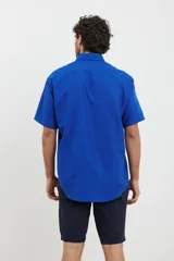 Camisa de manga corta azul con pequeños lunares blancos, cuello button-down y bolsillo en el pecho.