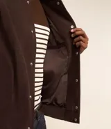 Campera bomber marrón de terciopelo pana con cuello redondo, cierre con botones a presión, bolsillos laterales, puños y cintura elastizados.