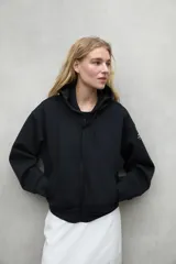 Campera negra con capucha ajustable con cordones, cierre frontal y bolsillos laterales.