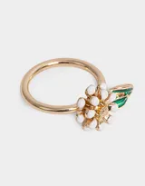 Anillo dorado con dije de flor con pétalos blancos y centro amarillo, y una hoja verde esmaltada.