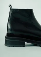 Bota corta de cuero negro, estilo botín chelsea, con puntera cuadrada y suela track gruesa y robusta.