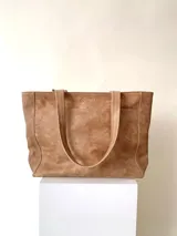 Cartera tipo tote de cuero graneado color negro, con textura uniforme y suave al tacto. Tiene manijas de 55 cm, bolsillo frontal con broche imantado, bolsillo trasero con cierre metálico, cierre principal metálico, forro interior y tres bolsillos internos (uno con cierre, uno plaqué y uno tipo sobre con solapa y botón).