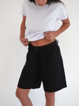 Bermuda negra de tiro medio, corte ancho, con bolsillos laterales y un ojal en la parte trasera.