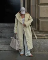 Abrigo trench maxi color beige con ribete de piel sintética en cuello y puños.