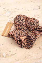 Scrunchie de poliéster con diseño de animal print en tonos tostados y negros, de textura ligera y delicada.