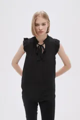 Blusa sin mangas color crudo con cuello con lazo y volados en los hombros.