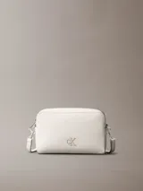 Cartera bandolera Calvin Klein color blanco, con correa ajustable, cierre de cremallera y logo CK metálico en el frente.