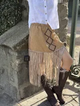 Falda midi confeccionada con tela de tapicería a rayas verticales en tonos grises y crudos, con apliques de cuero bordados a mano y flecos en el ruedo.