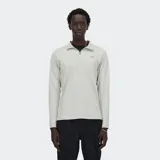 Buzo deportivo New Balance de manga larga, color gris claro jaspeado, con cuello polo y cierre frontal de un cuarto. Presenta trabillas para el pulgar en los puños y un logo reflectante NB en el pecho.