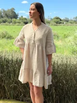 Vestido corto color beige de lino, con cuello mao, escote con botones, mangas 3/4 con volados y ruedo con volados.