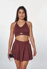 Conjunto deportivo color marrón compuesto por un top con cuello halter y logo blanco, y una minifalda tableada.