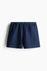 Short de denim azul oscuro, de corte holgado, con cintura elastizada y cordón de ajuste. Cuenta con bolsillos laterales y aberturas laterales en el ruedo.