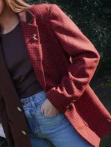 Blazer oversize con diseño asimétrico que combina dos tweeds contrastantes: uno marrón liso y otro blanco y negro con estampado pata de gallo. Tiene botones de strass y un pin de salchicha.