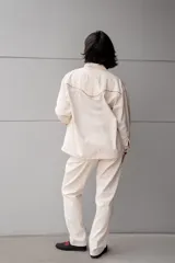 Chaqueta blanca de jean con cuello clásico, cierre frontal con botones metálicos y bolsillo de parche en el pecho. Presenta detalles de piedras de colores en el canesú.