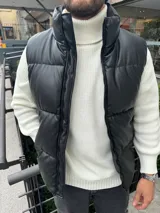 Chaleco puffer negro de cuero sintético con cierre frontal y cuello alto.