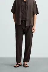 Pantalón de corte relajado (relaxed fit) color verde militar, confeccionado en mezcla de algodón y lino. Presenta cintura elástica ajustable con cordón y bolsillos frontales y traseros de vivo.