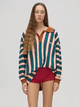 Chomba de corte oversize con cuello camisero, a rayas verticales en color marrón, lila y blanco. Tiene un logo bordado en el pecho y puños en color marrón.