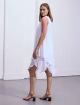 Vestido blanco de gasa con escote redondo bordado con apliques metálicos. Tiene forro interno a tono y ruedo en capas asimétricas.