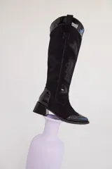 Bota bucanera negra de cuero, con detalles en charol y gamuza, diseño estilo western con punta fina y taco bajo.